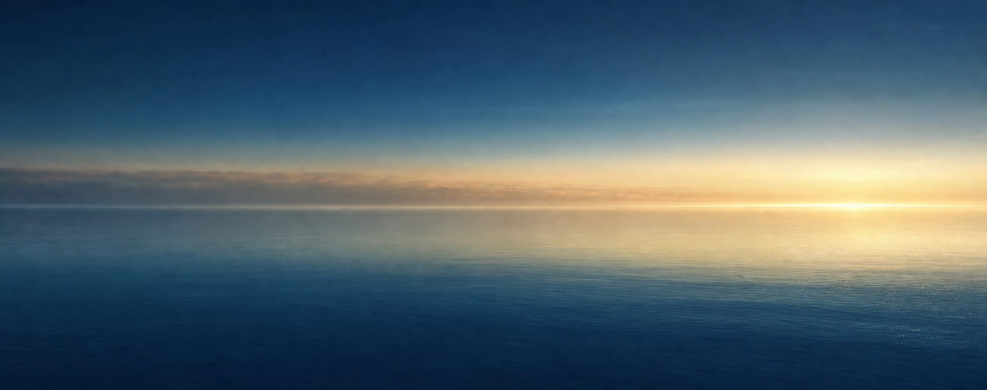 Layered bands of navy, teal and pale gold light over calm water at dawn